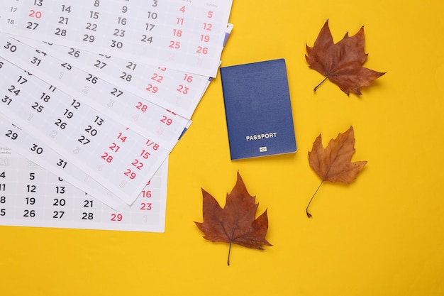 Kalender met gevallen herfstbladeren paspoort op gele achtergrond Herfst reizen Bovenaanzicht