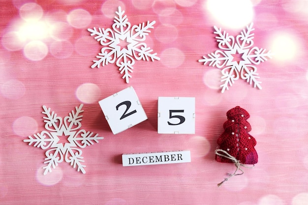 Kalender voor 25 december kubussen met het nummer 25 de naam van de maand in Engelse decoratieve sneeuwvlokken en een kerstboom op een roze achtergrond bokeh