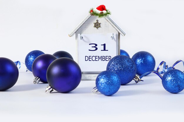 Kalender voor 31 december een decoratief huis met de naam december in het Engels het nummer 31 gekleed in een kerstman hoed tussen blauwe kerstboomversieringen lichte achtergrond