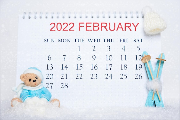 Kalender voor de maand februari 2022. notitieboekje met kalenderdata en een speelgoedteddybeer, blauwe ski's, witte hoed op sneeuw