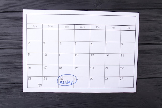 Kalenderdag gemarkeerd als een vakantie door een blauwe markering die een vakantie plant in een papieren kalender donker hout...