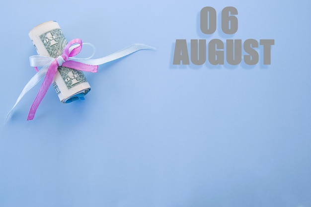Kalenderdatum op blauwe achtergrond met opgerolde dollarbiljetten vastgemaakt door blauw en roze lint 6 augustus