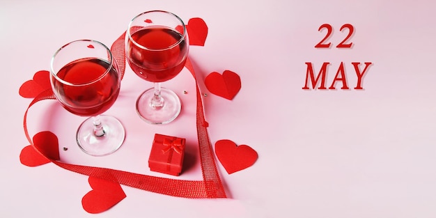 Kalenderdatum op lichte achtergrond met twee glazen rode wijn rode geschenkdoos en rode harten 22 mei