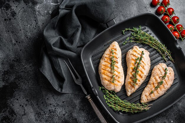 Kalkoen gegrilde borstfilet steaks in een koekenpan. Zwarte achtergrond. Bovenaanzicht. Ruimte kopiëren.