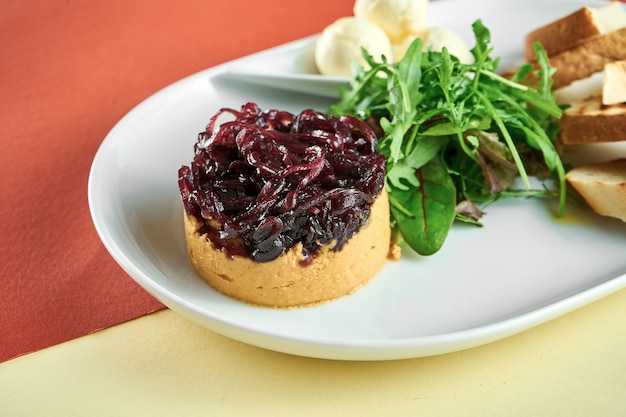 Kalkoenleverpastei met gekonfijte uien, curtons in een witte plaat op een felgekleurd oppervlak