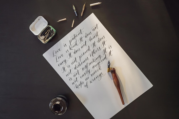 Kalligraaf handen schrijft zin op wit papier Bijbel zin over liefde Inscriptie sier versierde letters Kalligrafie grafisch ontwerp belettering handschrift creatie concept