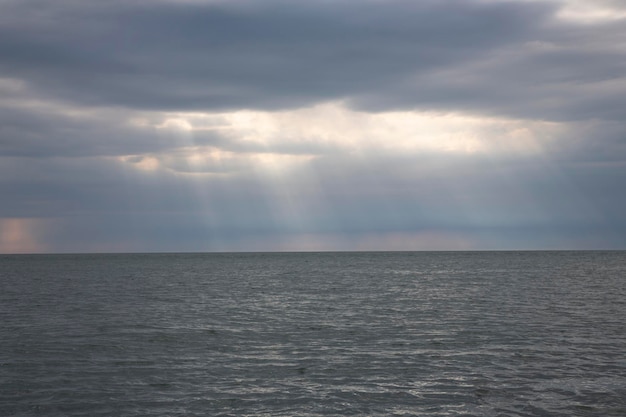 Kalm zeegezicht met stormachtige lucht waar zonnestralen door de wolken komen