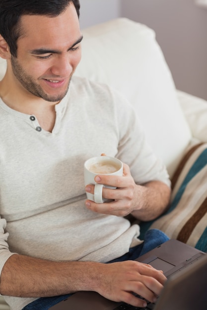 Kalme aantrekkelijke mens die koffie drinkt terwijl het gebruiken van zijn laptop