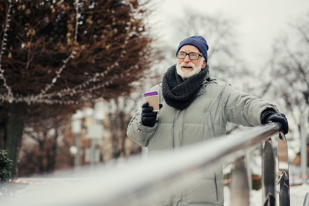 Kalme gepensioneerde gepensioneerde die alleen in het park loopt in de winter en een kartonnen kop warme chocolademelk vasthoudt