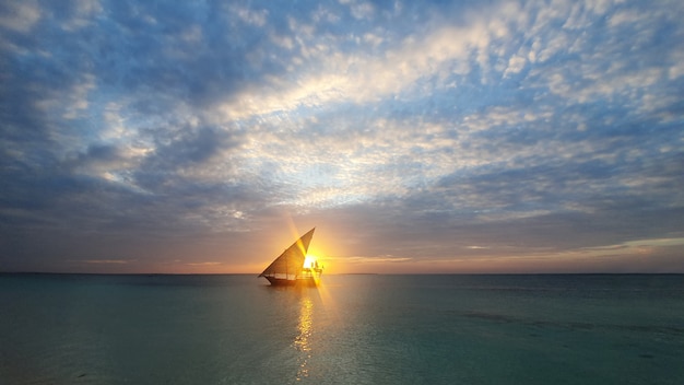 Kalme Indische Oceaan in de stralen van de ondergaande zon en de blauwe hemel met kleine wolken. een boot met een zeil gaat de oceaan op.