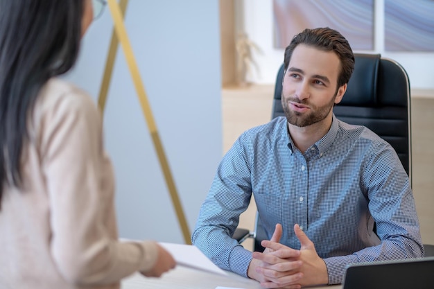 Kalme jonge CEO die aan tafel zit terwijl hij een gesprek voert met zijn vrouwelijke secretaresse
