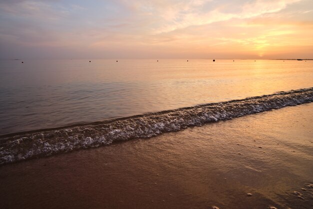 Kalme kust met verpletterende golven op zandstrand bij zonsopgang.