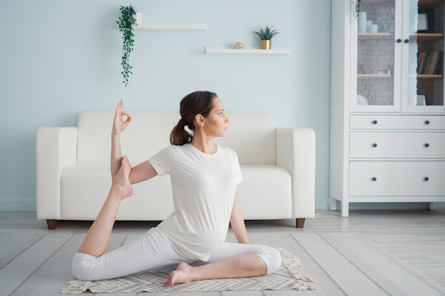 Kalme zwangere vrouw doet ardha matsyendrasana thuis poseren.