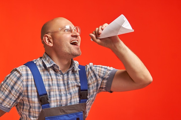 Foto kalve man in een werkpak en beschermende bril schreeuwt in een papieren luidspreker