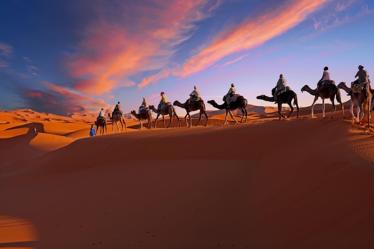 Foto kamelenkaravaan die bij zonsondergang door de sahara-woestijn in marokko rijdt