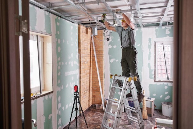 Kamer reparatie. Binnenafwerking. jonge bouwer maakt een gipsplaatplafond, staande op een trapladder