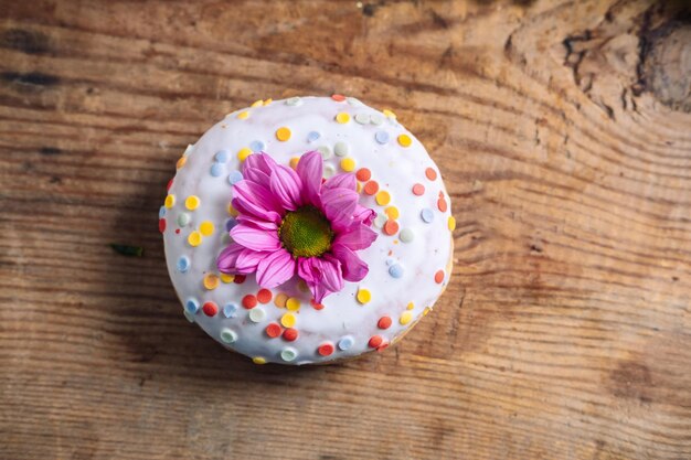 Foto kamille knop bovenop donut op houten achtergrond delicaat frame met roze bloem.