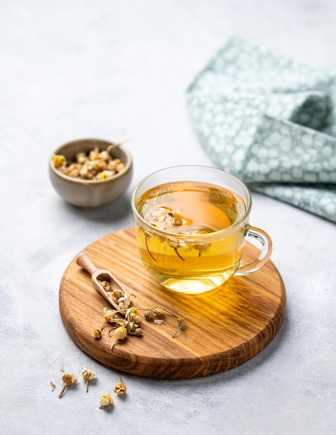 Foto kamille kruidenthee in een glazen beker op een houten plank op een lichte achtergrond met droge bloemen het concept van een gezonde detox drank voor gezondheid en slaap