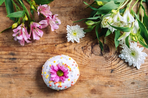 Kamilleknop bovenop een donut op een houten achtergrond met een boeket alstroemerias en chrysanthemums delicaat frame met roze bloem.