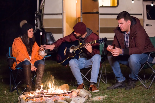 Kampeerders die op gitaar spelen en marshmallows roosteren op een camping in de bergen. retro camper.