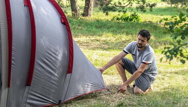 Kamperen, reizen, toerisme, wandelen concept - jonge man tent opzetten in het bos.