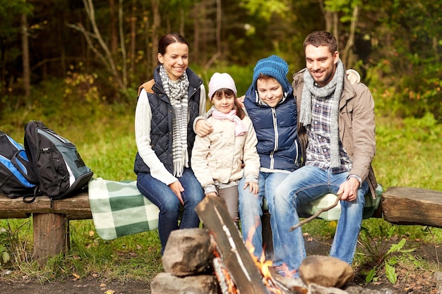 kamperen, reizen, toerisme, wandelen en mensen concept - gelukkige familie zittend op een bankje bij kampvuur in het bos