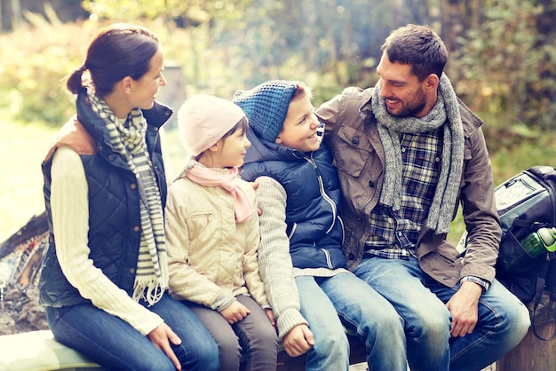 kamperen, reizen, toerisme, wandelen en mensen concept - gelukkige familie zittend op een bankje en praten in het kamp in het bos