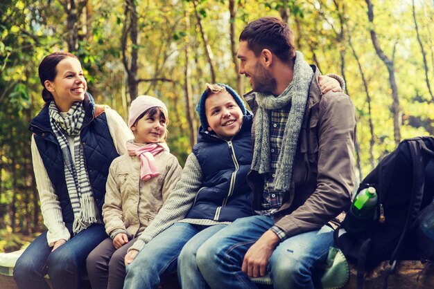 kamperen, reizen, toerisme, wandelen en mensen concept - gelukkige familie zittend op een bankje en praten in het kamp in het bos