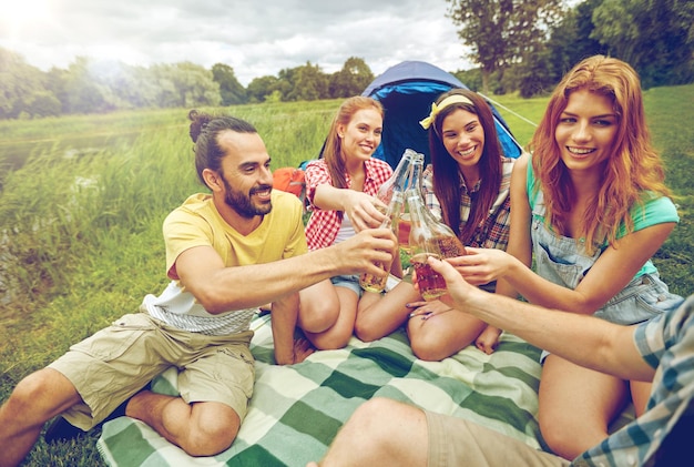 kamperen, reizen, toerisme, wandelen en mensenconcept - gelukkige vrienden met glazen flessen die cider of bier drinken op de camping