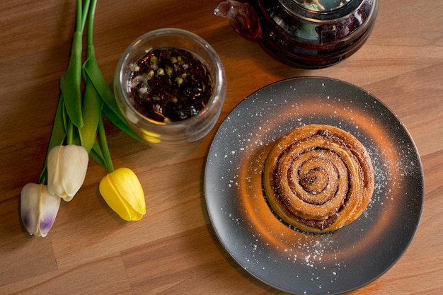 Kaneelbroodjes met suikerpoeder en gele tulpen op een houten tafel