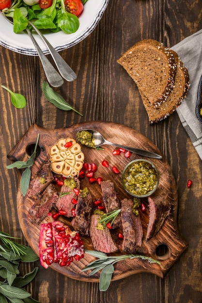 Kangaroo meat steak with green pesto and pomegranate on wooden cutting board. 