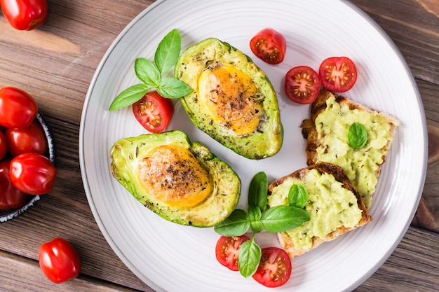 Kant-en-klaar voorgerecht gebakken avocado met ei, toast en cherrytomaatjes op een bord op een houten tafel. Gezond eten. Flexitarisch dieet. Bovenaanzicht. Detailopname