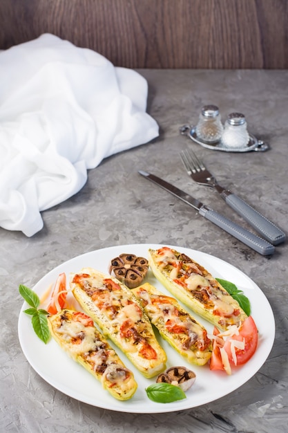 Kant-en-klare gebakken courgette helften gevuld met kaas en tomaat en basilicum blaadjes op een bord op tafel. Plantaardige gerechten, gezonde voeding. Verticale weergave