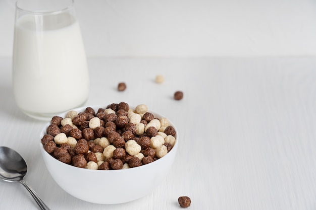 Kant-en-klare gezonde granen in kom geserveerd met lepel en glas melk voor het ontbijt op tafel