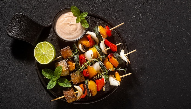 Kant-en-klare veganistische kebabs van groenten en gerookte tofu met cashewsaus en gerookte paprika op een zwarte