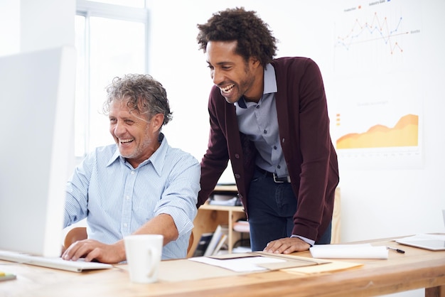 Kantoor capriolen Twee collega's in een kantoor lachen om iets dat ze op internet hebben gevonden