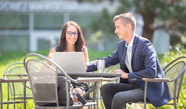 Kantoor mannelijke en vrouwelijke collega's bespreken werk over een opengeklapte laptop en een afhaalmaaltijden koffiekopje buitenshuis.