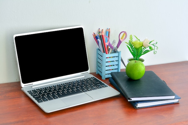 Foto kantoorbenodigdheden, laptop met notitieboekje en appel op houten tafel