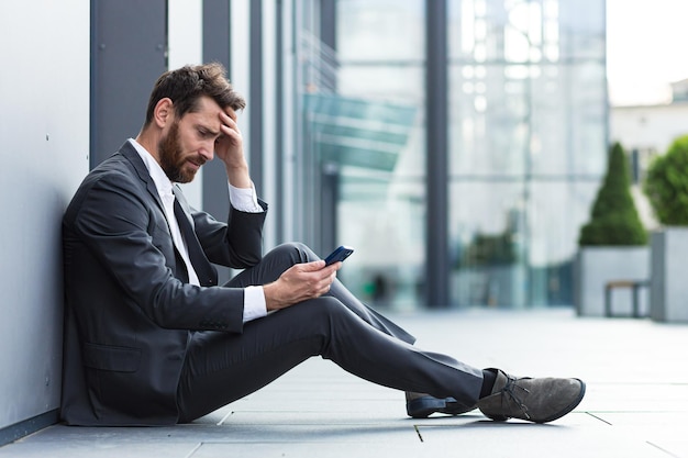 Kantoormedewerker die buiten in de buurt van kantoor zit, kreeg slecht nieuws, depressief en moe leest slecht nieuws van de telefoon online