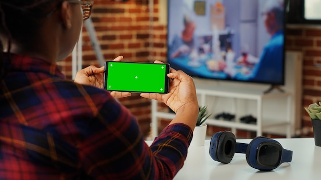 Kantoormedewerker kijkt naar horizontale greenscreen op smartphone, met behulp van mockup lege copyspace met chroma key tentoongesteld. telefoon houden met geïsoleerde kopie ruimte sjabloon in appartement.