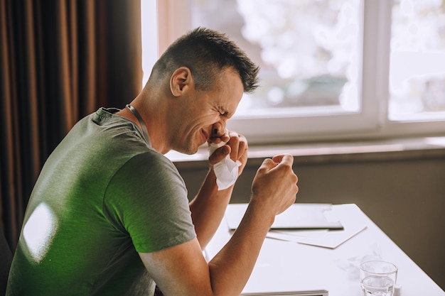 Kantoormedewerker zit aan tafel en niest