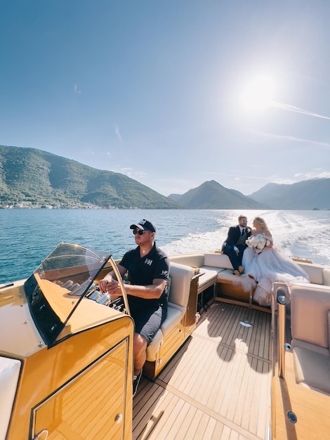 Kapitein zit aan het roer van het jacht met de bruid en bruidegom aan boord drijvend op de zee