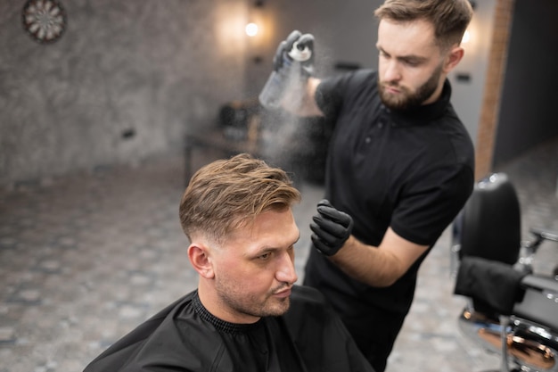 Kapper brengt haarlak aan op het haar van een mannelijke cliënt die in een stoel in de kapperszaak zit