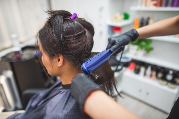 Kapper die een haar gebruikt dat is rechtgetrokken om het haar recht te trekken haarstylist die aan de haarstijl van een vrouw werkt bij salonhaarverzorging mooie aantrekkelijke vrouw in een schoonheidssalon