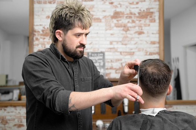 Kapper die haar met een schaar knipt voor een knappe jonge man Fotografie van hoge kwaliteit