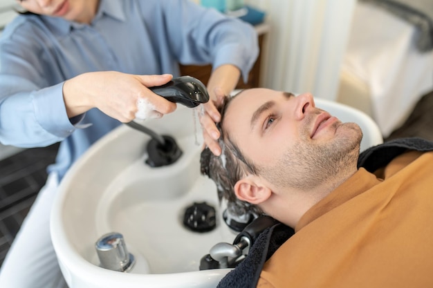 Kapper die haar wast aan de mannelijke cliënt in een schoonheidssalon