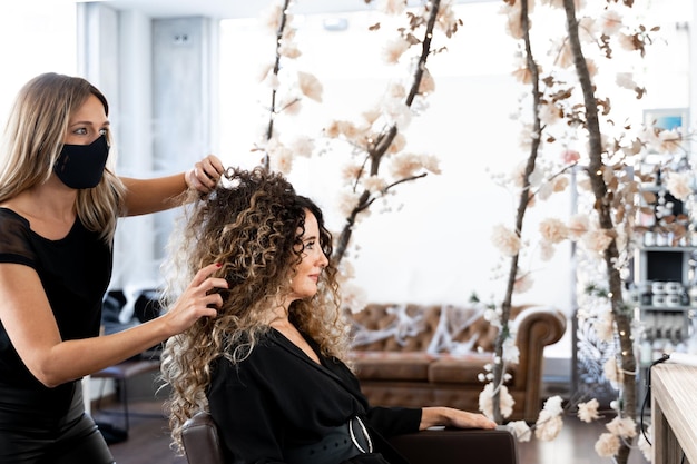 Kapper die het krullende haar van een vrouw voor een spiegel in een salon fixeert