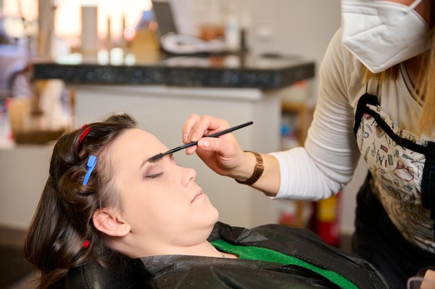 kapper die make-up doet en een jonge vrouwelijke cliënt in een schoonheidssalon stileert