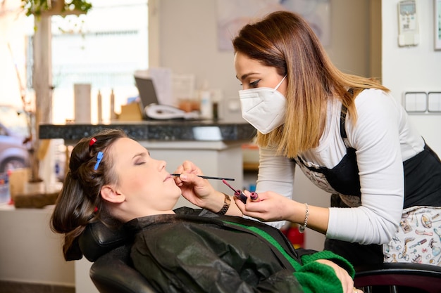 kapper die make-up doet en een jonge vrouwelijke cliënt in een schoonheidssalon stileert