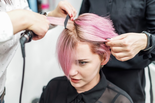 Kapper die roze haar met haarijzers rechtmaakt.